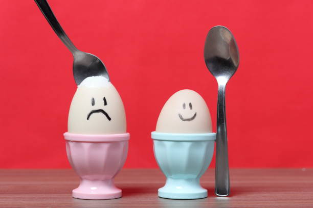 istock A boiled egg with a chopped shell stands in a poached. On the egg painted smiley. A spoon is stuck in it for food. Against the background of coral color. 1160262188
