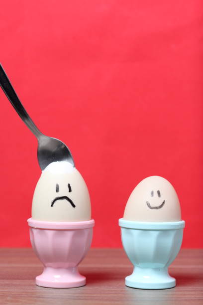 istock A boiled egg with a chopped shell stands in a poached. On the egg painted smiley. A spoon is stuck in it for food. Against the background of coral color. 1160262189
