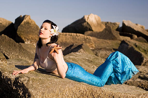 Young woman with starfish in hand lying on rocks stock photo