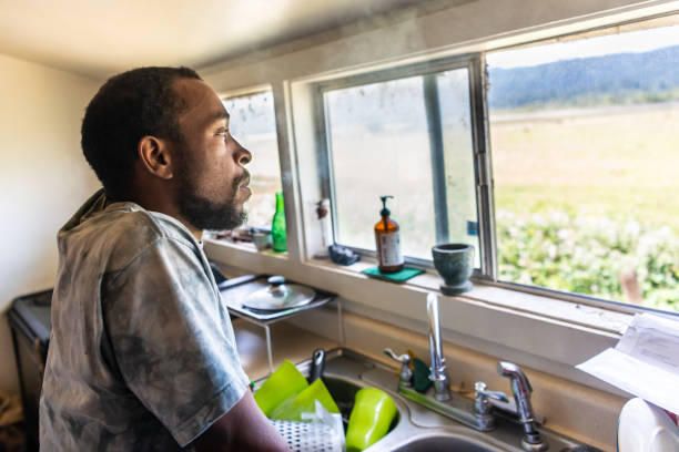 Serious black mid adult man looking through a window Serious afro caribbean mid adult man looking through a window at his home kitchen mid adult men stock pictures, royalty-free photos & images