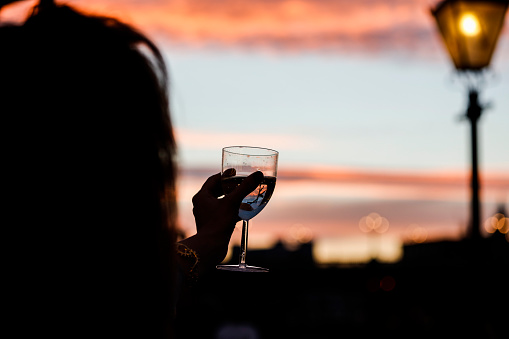Silhouettes of woman drink glasses of champagne wine at sunset dramatic sky