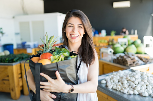 Portrait of good looking customer holding organic veggies and fruits in bag at supermarket