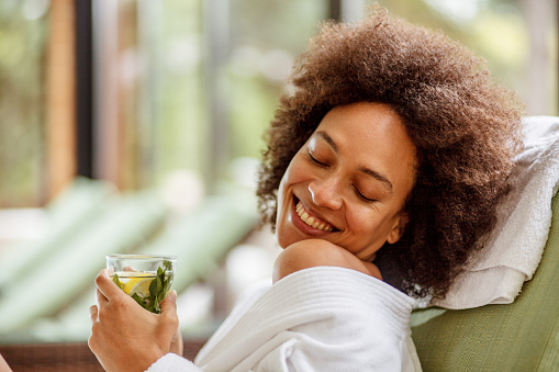Smiling young woman relaxing in a cozy bathrobe while enjoying a refreshing herbal tea on her weekend getaway at the wellness resort.