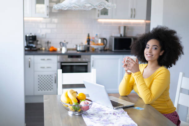 istock African woman drinking coffee at home and using laptop 1160297225
