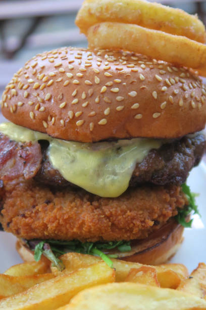 istock Image of gourmet beefburger / hamburger in burger bun with sesame seeds, melted cheese, bacon rasher, deep-fried halloumi cheese in breadcrumbs, lettuce and battered onion rings, served with French fries, crispy chunky chips pub grub food in beer garden 1160307763