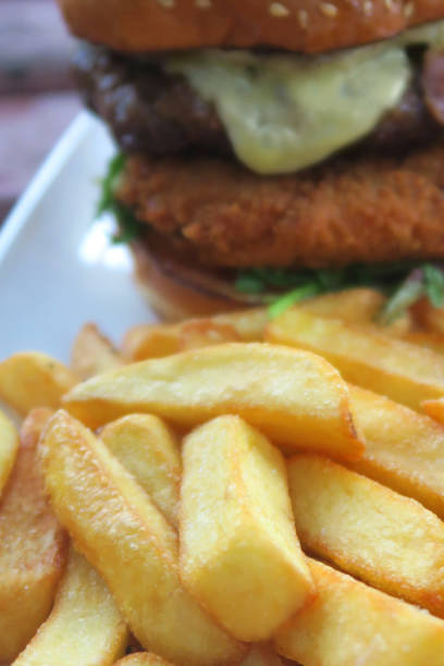 istock Image of gourmet beefburger / hamburger in burger bun with sesame seeds, melted cheese, bacon rasher, deep-fried halloumi cheese in breadcrumbs, lettuce and battered onion rings, served with French fries, crispy chunky chips pub grub food in beer garden 1160312995
