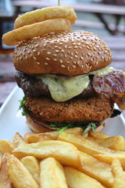istock Image of gourmet beefburger / hamburger in burger bun with sesame seeds, melted cheese, bacon rasher, deep-fried halloumi cheese in breadcrumbs, lettuce and battered onion rings, served with French fries, crispy chunky chips pub grub food in beer garden 1160312997