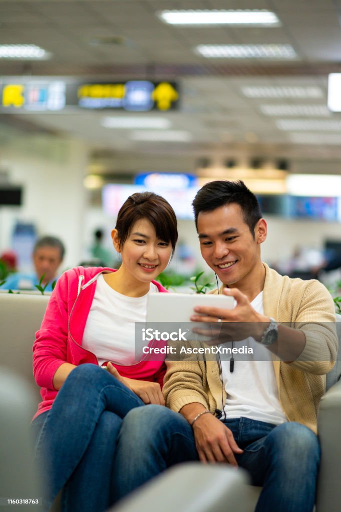 Couple wathcing a movie in an airport lounge Smiling couple taking selfie from digital tablet. Happy man and woman are sitting in waiting room at airport. They are going on vacation. 25-29 Years Stock Photo