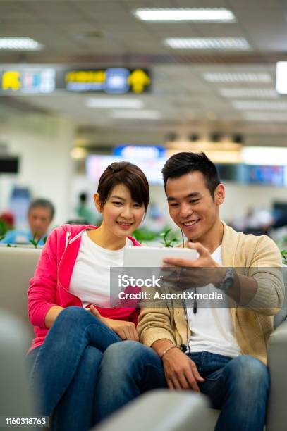 Couple Wathcing A Movie In An Airport Lounge Stock Photo - Download Image Now - 25-29 Years, 30-34 Years, Adult