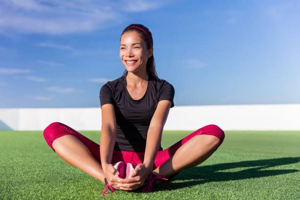 glückliche fitness asiatische frau dehnt beine im park - floor women sitting yoga stock-fotos und bilder