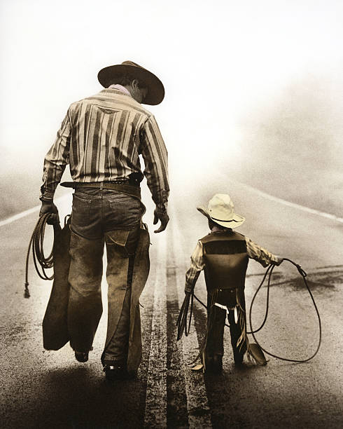 Learning the Ropes A Cowboy father teaches his son the ropes. Together they walk a lonely highway on a foggy morning. cowboy photos stock pictures, royalty-free photos & images