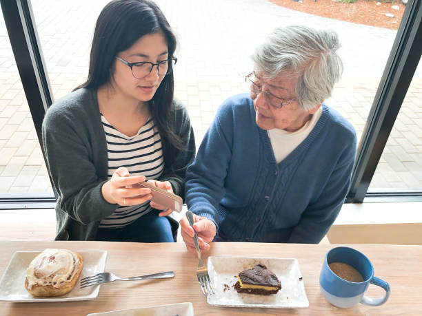 barnbarn visar mormor smartphone medan du äter desserter på coffee shop - cinnamon buns people bildbanksfoton och bilder