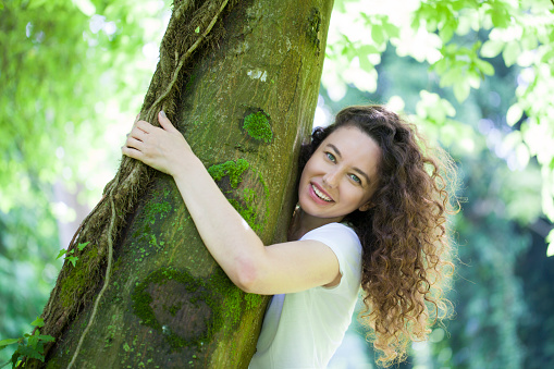 Casual cheerful brunette embracing a tree in a park on sunny day