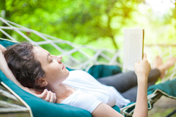 istock Young woman relaxing in hammock with book 1160355288
