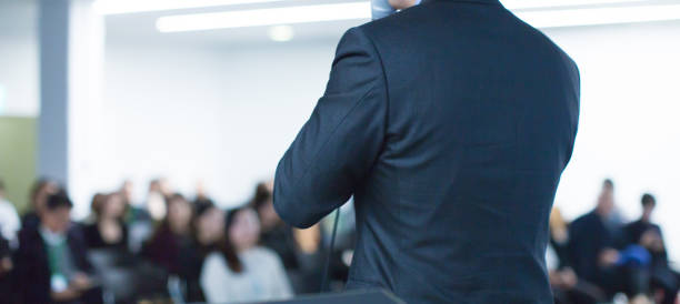 Speaker at conference giving a talk about corporate business. Audience in hall with presenter giving presentation. Seminar lecture with corporate executive giving speech during business workshop. stock photo
