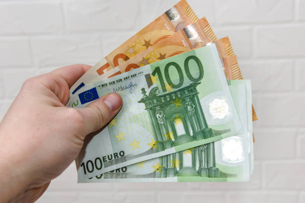 istock Hand with euro banknotes upon white brick wall close up 1160364093