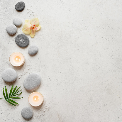 Spa concept on white stone background, palm leaves, flowers, candles and zen like grey stones, top view, copy space.