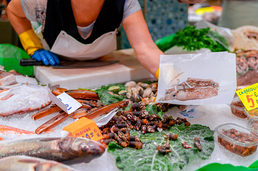 El vendedor en el mercado de pescado ofrece calamares frescos al cliente. Colores brillantes, enfoque selectivo, bokeh photo