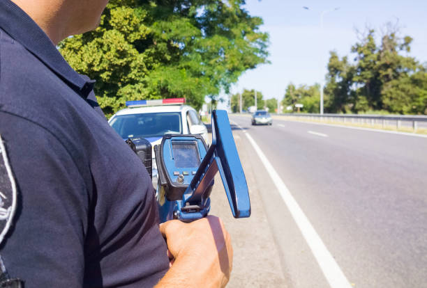 polícia que prende o injetor de velocidade do laser perto do carro de polícia no fundo da estrada. foco seletivo, parte do corpo. - ticket control - fotografias e filmes do acervo