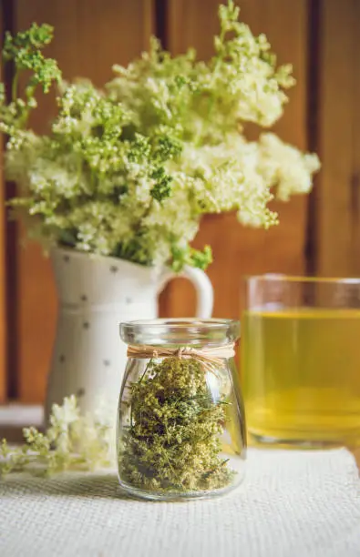 Fresh Meadowsweet, Filipendula ulmaria in jug shape vase and it`s herbal tea in glass, tea powder in jar. Indoors country home house.
