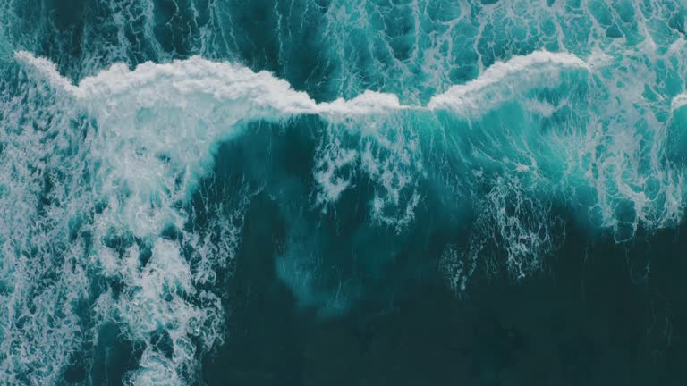 Aerial view ocean waves break into foam along the shore