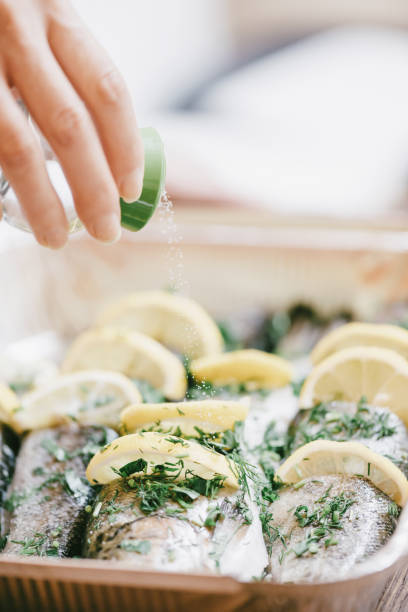 Two baked sea breams with sliced lemon and potatoes on the brown oval plate, wooden background