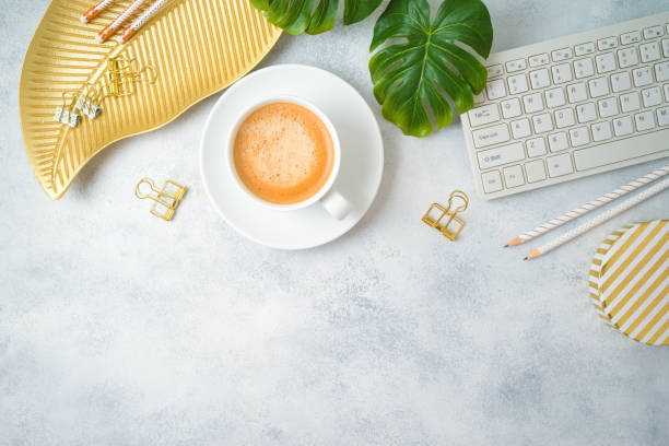 istock Flat lay home office feminine table with coffee cup, golden accessories, computer keyboard and tropical leaves on grey background. Top view from above 1160405020