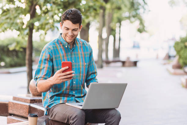 istock Cheerful man using laptop and smartphone in a city 1160409329