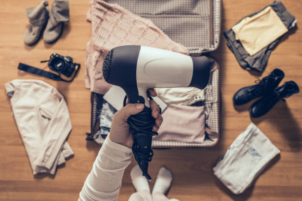 Top view on the woman holds hair dryer packing clothes in the open suitcase. Travel concep stock photo