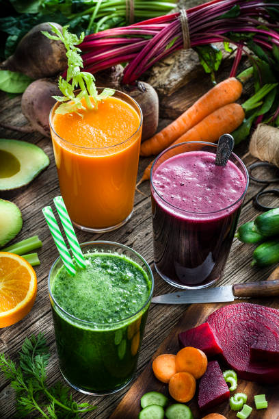 Vegetable drinks: high angle view of three drinking glasses filled with beet, carrot and green vegetables juice shot on rustic wooden kitchen table. Vegetables like beet, carrots, cucumber, broccoli, avocado and celery are all around the juice glasses. Predominant colors are purple, green and orange. Low key DSRL studio photo taken with Canon EOS 5D Mk II and Canon EF 100mm f/2.8L Macro IS USM.