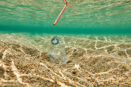 Used plastic single use water bottle with red straw in the ocean. Staged pollution image.