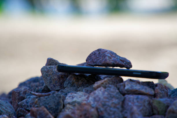 Cell phone with broken glass on gravel granite stones, unbreakable gadget.