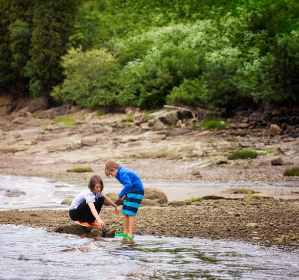Little boys is sitting next to river and play with rocks
