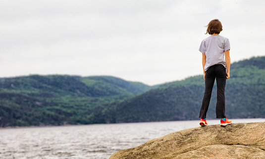 Preteen girl standing on a rock looking at Saguenay River pensively.