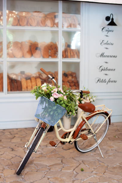 vintage gelbes fahrrad mit einem korb mit blumen steht in der nähe des cafés einer bäckerei vor dem hintergrund des hölzernen blauen hauses. sommerstimmung. öko-transport. fahrrad mit blumentopf, hochzeitsblume - bicycle ornamental garden flower formal garden stock-fotos und bilder