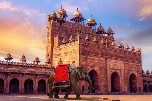 Agra, India, March 16, 2018: Decorated elephant used for tourist ride near Buland Darwaza Fatehpur Sikri Agra. A beautifully crafted giant red sandstone gateway to Fatehpur Sikri. A UNESCO World Heritage site at Agra, Uttar Pradesh, India.