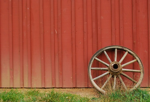 A wooden wagon wheel rests against a red barn