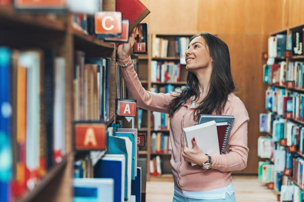 istock Young woman searching books in the library 1160444896