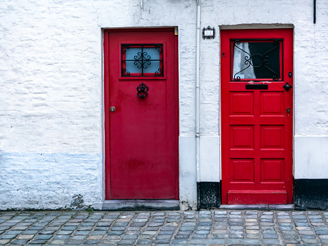 Two red wooden front doors in the white brick wall. Two vintage red doors with window at the top.