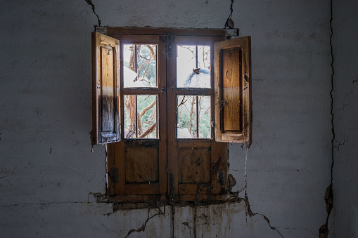 Old door and window in an abandoned building. Background scene of a vintage interior space with wallpaper. Paint is peeling off the walls and a lot of dirt is lying around.