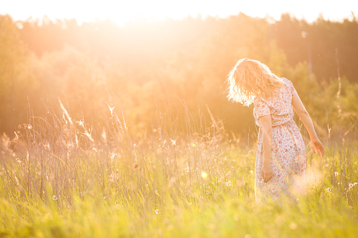 Portrait of happy young blond woman running on a meadow on a sunny summer day. Girl dancing on the grass in the park. Outdoors. Cheerful woman on sunset. Lifestyle and happiness concept