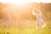 Portrait of happy young blond woman running on a meadow on a sunny summer day. Girl dancing on the grass in the park. Outdoors. Cheerful woman on sunset. Lifestyle and happiness concept