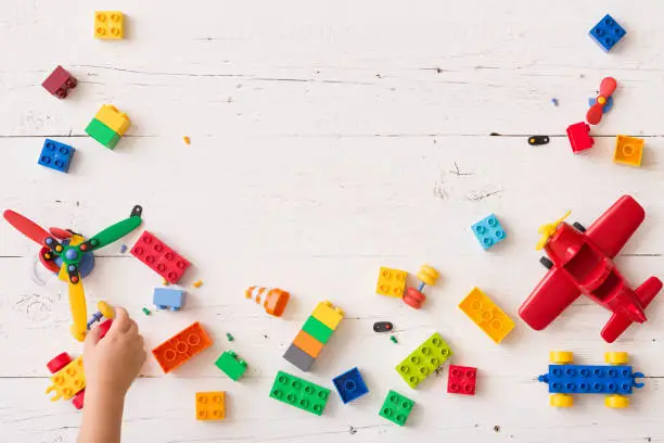 Photo of Top view on child's hand playing with multi-color plastic bricks at the table. Toddler having fun and building out of bright constructor bricks. Early learning. Developing toys