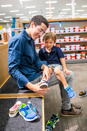 young man shopping for shoes for his son sitting in a department store bench