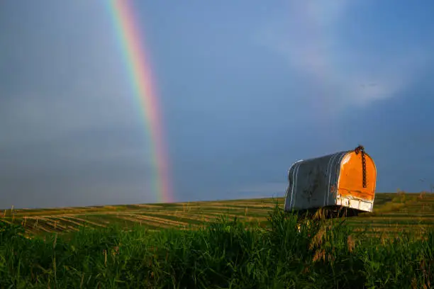 Photo of Rusty mailbox with rainbow and cornfield against blue sky