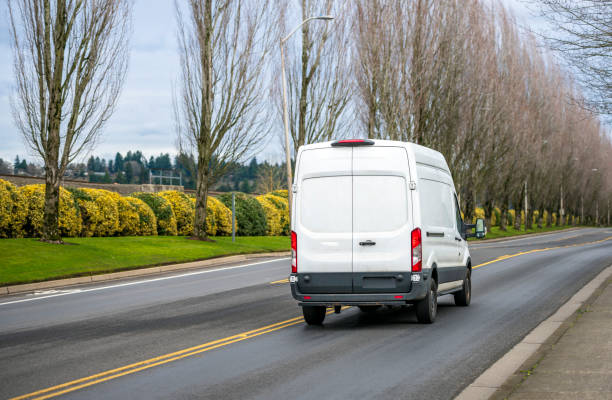 木の路地で道路上を走る白いコンパクトな商用貨物ミニバン - car delivering white mini van ストックフォトと画像