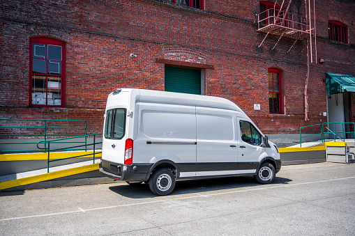 White compact popular commercial economical cargo mini van for local deliveries and business specifications standing on the warehouse parking lot on the city street
