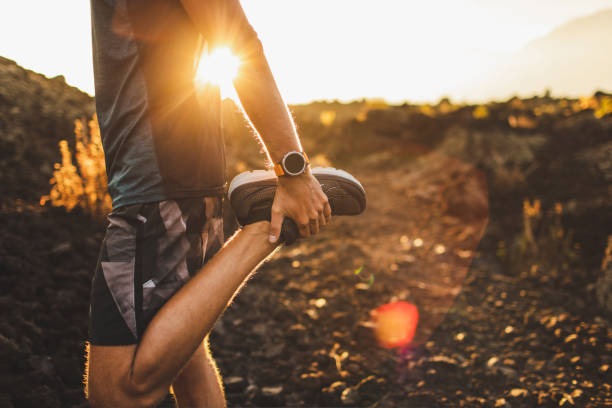 男性ランナーは足と足を伸ばし、屋外で走る準備をします。手元のスマートウォッチやフィットネストラッカー。背景に美しい太陽の光。アクティブで健康的なライフスタイルのコンセプト� - mens sports ストックフォトと画像