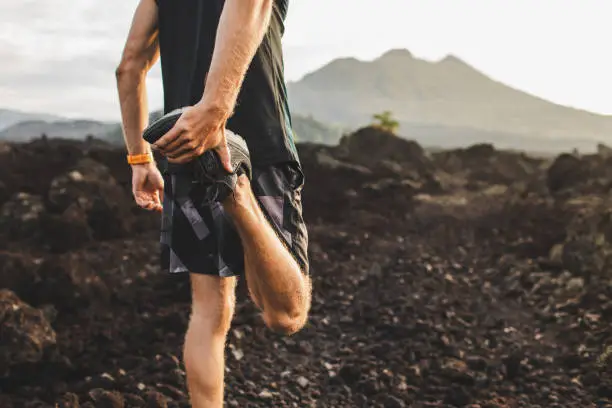 Runner stretching leg and feet and preparing for trail running outdoors. Active and healthy lifestyle concept. Mountain view on background.