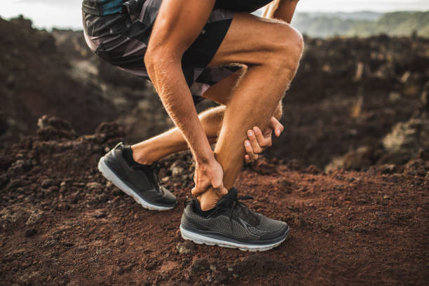 Achilles injury on running outdoors. Man holding Achilles tendon by hands close-up and suffering with pain. Sprain ligament or Achilles tendonitis. stock photo